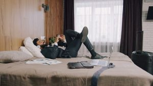 A man in a suit relaxing on a hotel bed with a laptop